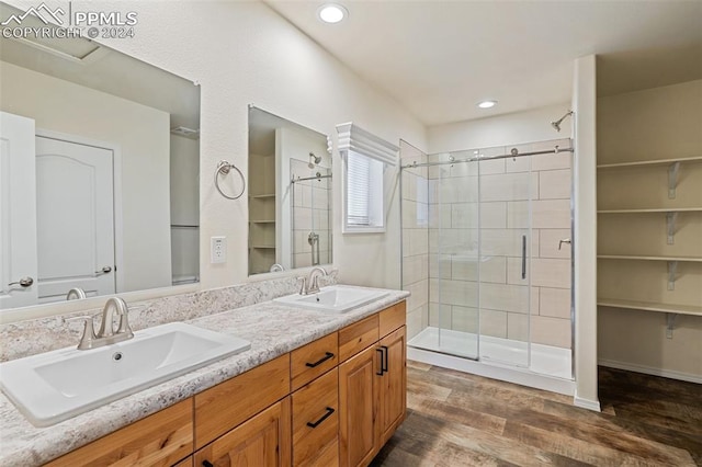 bathroom with double vanity, a shower with shower door, and wood-type flooring