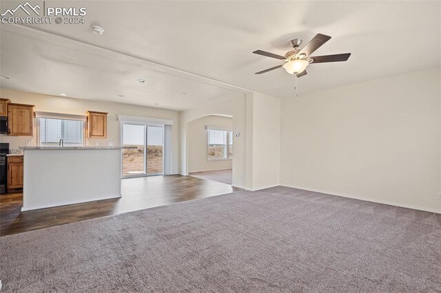 unfurnished living room featuring dark carpet, ceiling fan, and sink