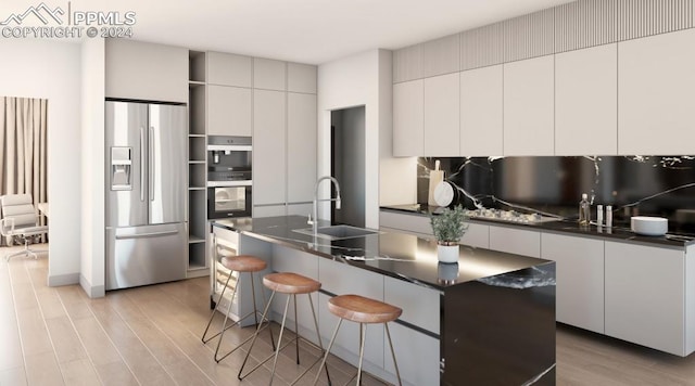 kitchen with light wood-type flooring, an island with sink, a breakfast bar, stainless steel appliances, and sink