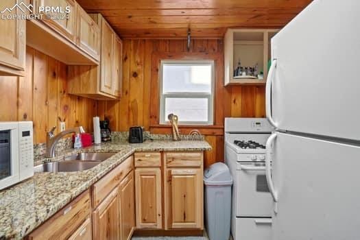 kitchen featuring wood walls, wooden ceiling, white appliances, sink, and light stone counters