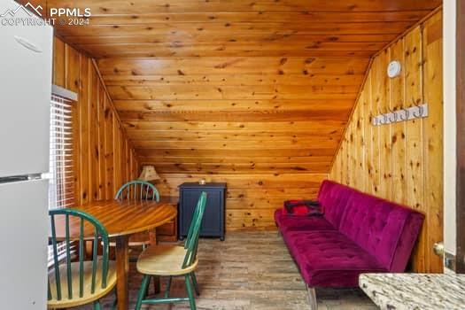 dining room with wood walls, vaulted ceiling, wooden ceiling, and wood-type flooring