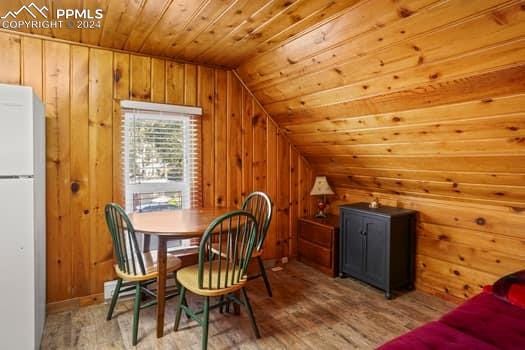 dining area featuring light hardwood / wood-style floors, wood ceiling, wooden walls, and lofted ceiling