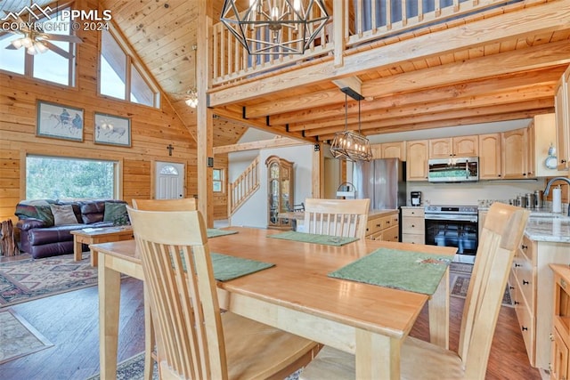 dining space featuring wood walls, high vaulted ceiling, ceiling fan with notable chandelier, light hardwood / wood-style flooring, and sink