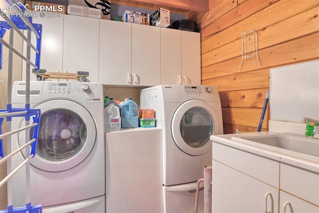 washroom featuring sink, wood walls, washer and dryer, and cabinets