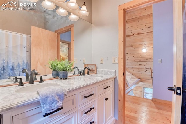 bathroom featuring wood-type flooring, oversized vanity, wooden walls, and dual sinks