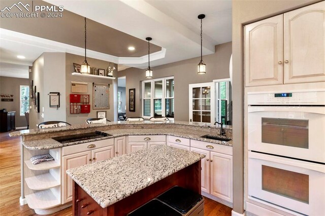 kitchen featuring sink, a raised ceiling, hanging light fixtures, white double oven, and light wood-type flooring