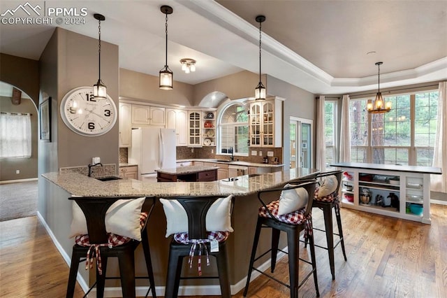 kitchen with a tray ceiling, a notable chandelier, light hardwood / wood-style flooring, white refrigerator, and pendant lighting