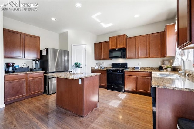 kitchen featuring sink, light stone counters, a center island, hardwood / wood-style flooring, and black appliances