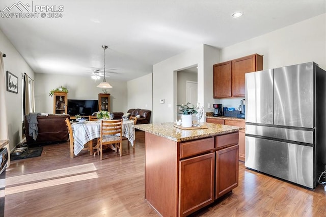 kitchen featuring a kitchen island, stainless steel fridge, hanging light fixtures, light hardwood / wood-style floors, and light stone countertops