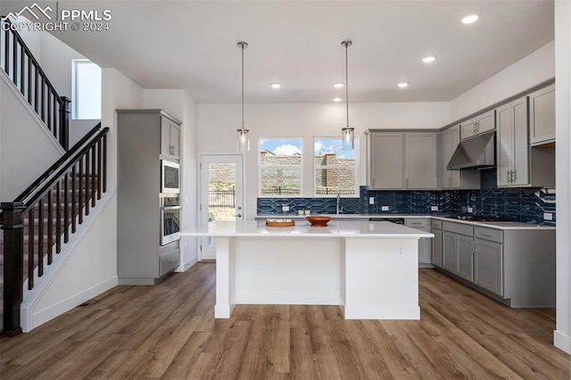 kitchen featuring a center island, stainless steel appliances, decorative light fixtures, gray cabinets, and hardwood / wood-style flooring