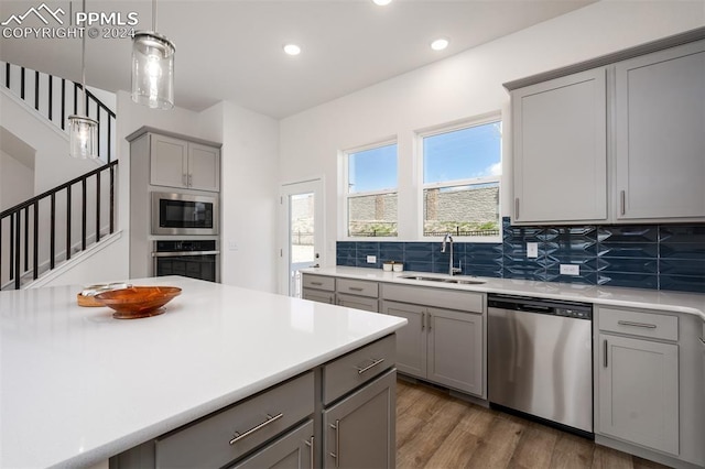 kitchen with tasteful backsplash, stainless steel appliances, sink, decorative light fixtures, and gray cabinets