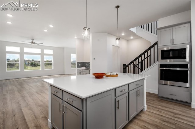 kitchen with ceiling fan, decorative light fixtures, gray cabinets, a kitchen island, and appliances with stainless steel finishes