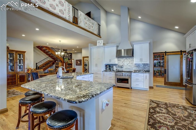 kitchen featuring a breakfast bar, stainless steel appliances, wall chimney range hood, and white cabinets