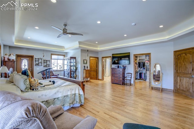 bedroom with a tray ceiling, a spacious closet, light hardwood / wood-style floors, and ceiling fan