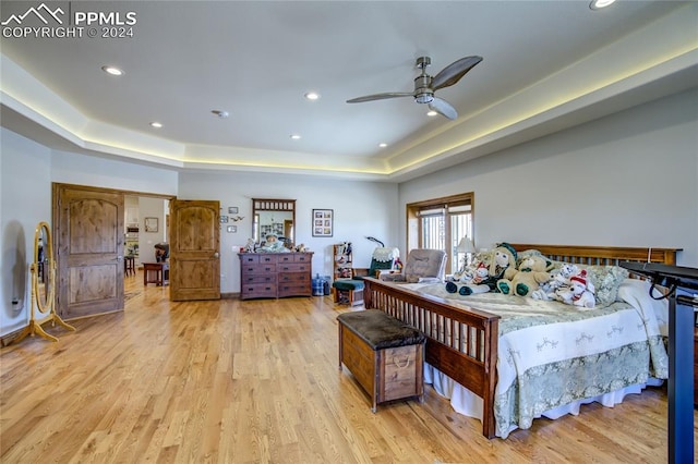 bedroom featuring ceiling fan, light hardwood / wood-style flooring, and a raised ceiling