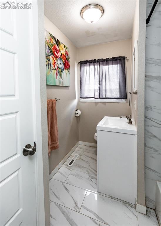 clothes washing area with sink, light tile floors, and a textured ceiling