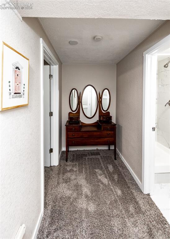 hall featuring a textured ceiling and dark carpet