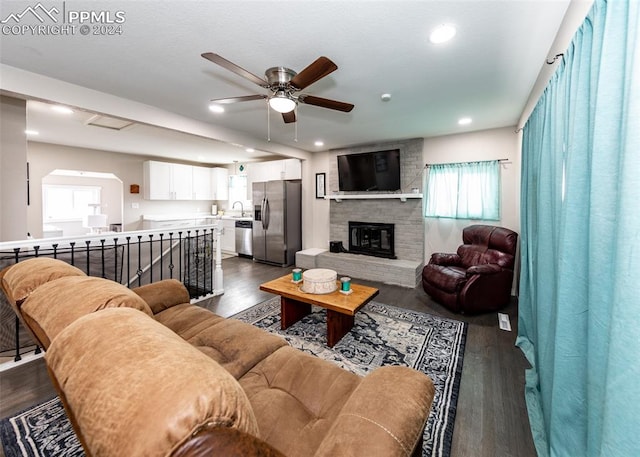 living room featuring dark hardwood / wood-style flooring, ceiling fan, sink, and a brick fireplace