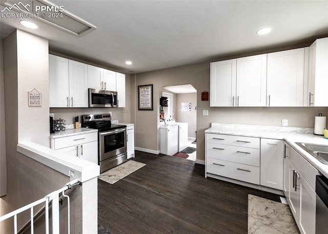 kitchen featuring appliances with stainless steel finishes, washer and dryer, white cabinetry, and dark hardwood / wood-style flooring