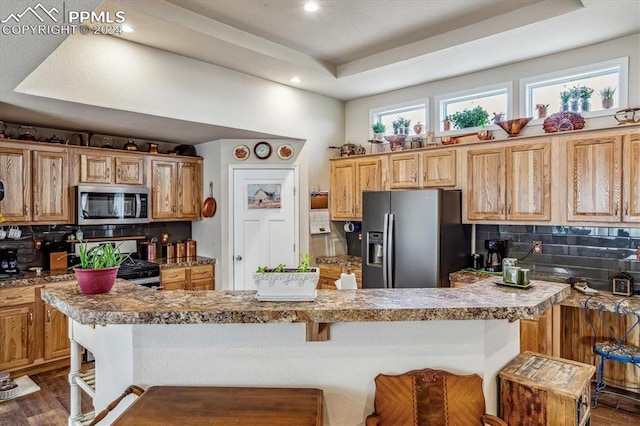 kitchen featuring decorative backsplash, a kitchen bar, stainless steel appliances, and dark wood-type flooring