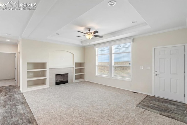 unfurnished living room featuring ceiling fan, carpet flooring, a tile fireplace, ornamental molding, and a tray ceiling