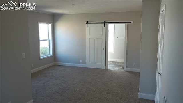 carpeted spare room featuring a barn door and crown molding