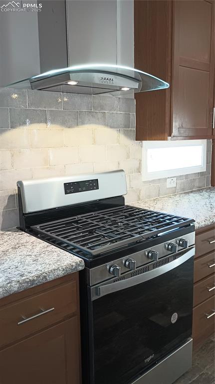 kitchen with wall chimney exhaust hood, light stone countertops, backsplash, and stainless steel gas range