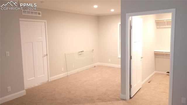 interior space with light colored carpet, a walk in closet, crown molding, and a closet