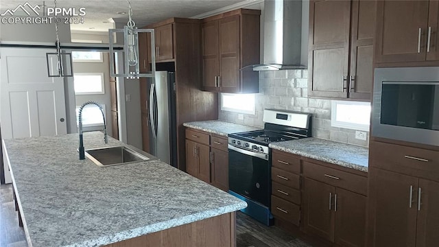 kitchen featuring sink, wall chimney range hood, stainless steel appliances, and a kitchen island with sink