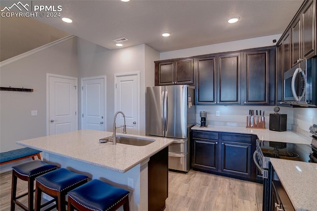 kitchen with appliances with stainless steel finishes, sink, light stone counters, light wood-type flooring, and a center island with sink