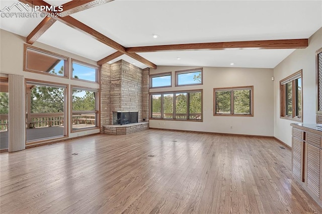 unfurnished living room featuring beamed ceiling, light hardwood / wood-style flooring, a stone fireplace, and high vaulted ceiling