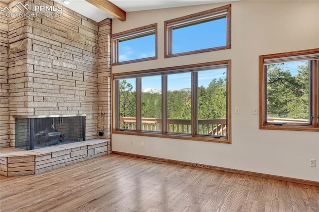 unfurnished living room with a stone fireplace, light hardwood / wood-style flooring, and vaulted ceiling with beams