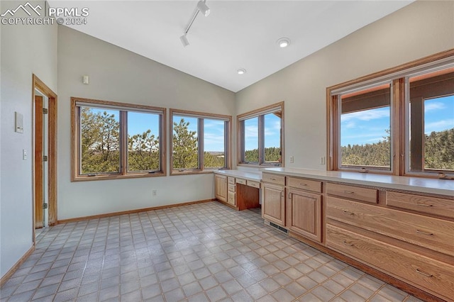 kitchen with vaulted ceiling, built in desk, light tile flooring, and rail lighting