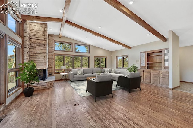 living room with beamed ceiling, high vaulted ceiling, hardwood / wood-style flooring, and a stone fireplace