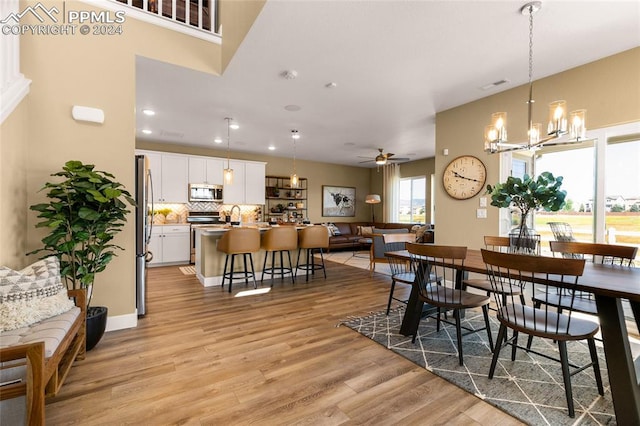 dining area with ceiling fan with notable chandelier and light hardwood / wood-style floors