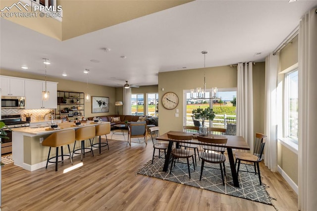 dining space featuring ceiling fan with notable chandelier, light hardwood / wood-style floors, and sink