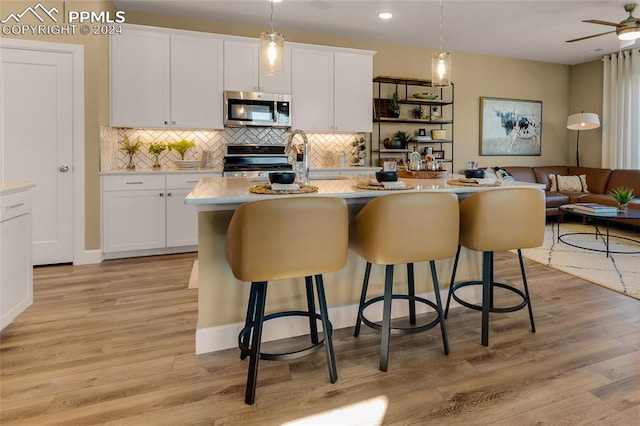 kitchen with pendant lighting, a kitchen island with sink, stainless steel appliances, ceiling fan, and light wood-type flooring