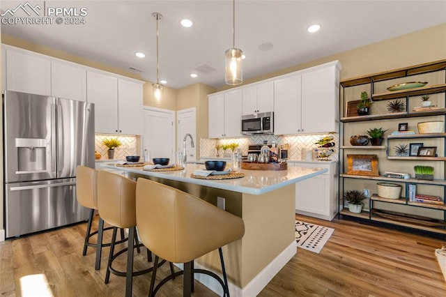 kitchen with white cabinets, appliances with stainless steel finishes, light hardwood / wood-style floors, an island with sink, and pendant lighting