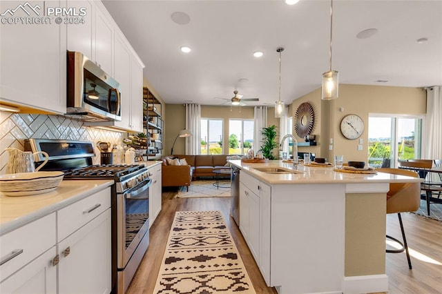 kitchen with hanging light fixtures, plenty of natural light, stainless steel appliances, and a center island with sink