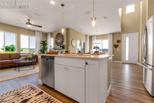 kitchen with white cabinets, appliances with stainless steel finishes, wood-type flooring, ceiling fan, and a kitchen island with sink