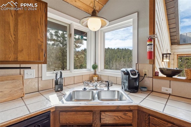 kitchen featuring sink, black dishwasher, tile counters, and pendant lighting