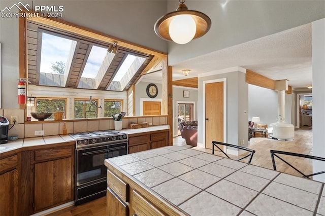 kitchen with pendant lighting, lofted ceiling with skylight, hardwood / wood-style flooring, black gas range, and tile countertops