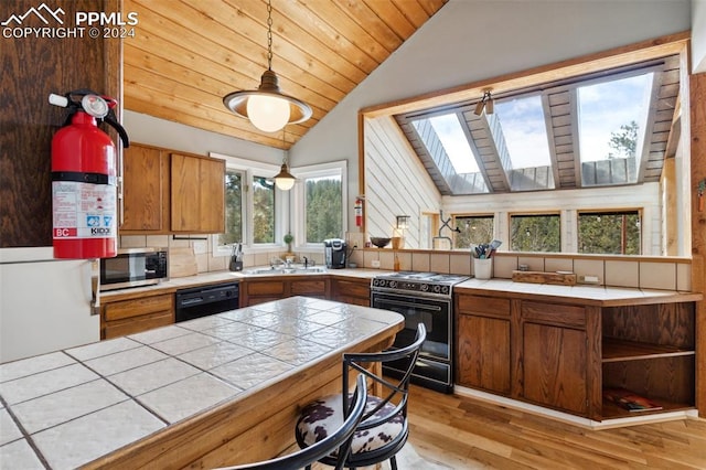 kitchen featuring sink, hanging light fixtures, vaulted ceiling with skylight, black appliances, and light hardwood / wood-style flooring