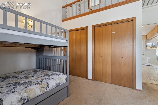 bedroom featuring light colored carpet, two closets, and a towering ceiling