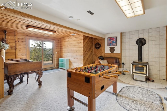 rec room with wooden walls, a wood stove, light colored carpet, and tile walls