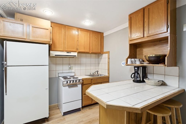 kitchen with white appliances, tasteful backsplash, light wood-type flooring, a breakfast bar area, and tile countertops