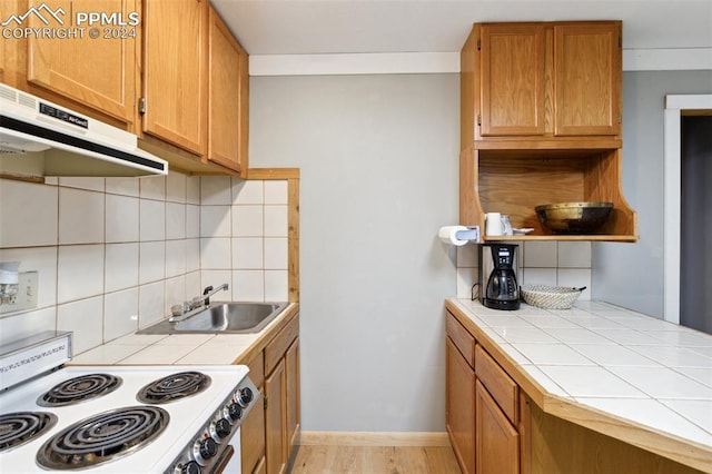 kitchen with backsplash, tile counters, range, sink, and light wood-type flooring