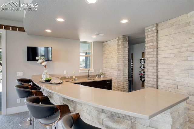 kitchen featuring kitchen peninsula, a textured ceiling, carpet, sink, and a breakfast bar