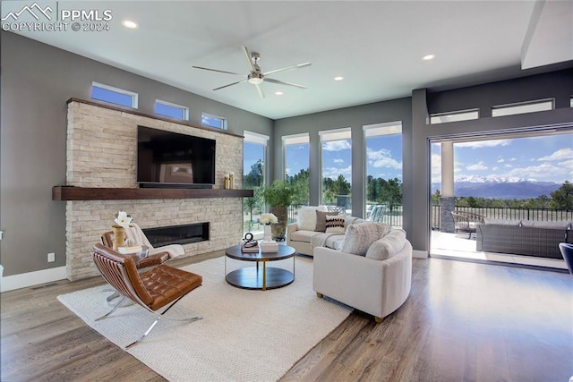 living room with a stone fireplace, a healthy amount of sunlight, hardwood / wood-style flooring, and ceiling fan