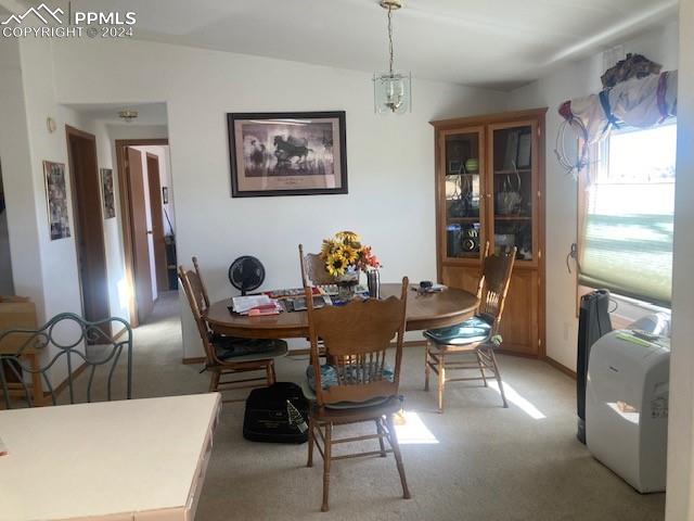 dining area featuring light colored carpet, lofted ceiling, and a notable chandelier